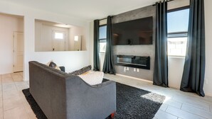 A modern living room with a grey sofa, a black rug, and a large window with dark curtains. - Sunny Arizona Escape w/ Patio, Grill & Fireplace! (Glendale)