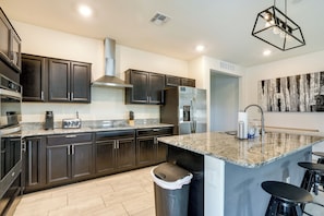 A modern kitchen with dark cabinets, granite countertops, stainless steel appliances, and a central island with bar stools. - Sunny Arizona Escape w/ Patio, Grill & Fireplace! (Glendale)