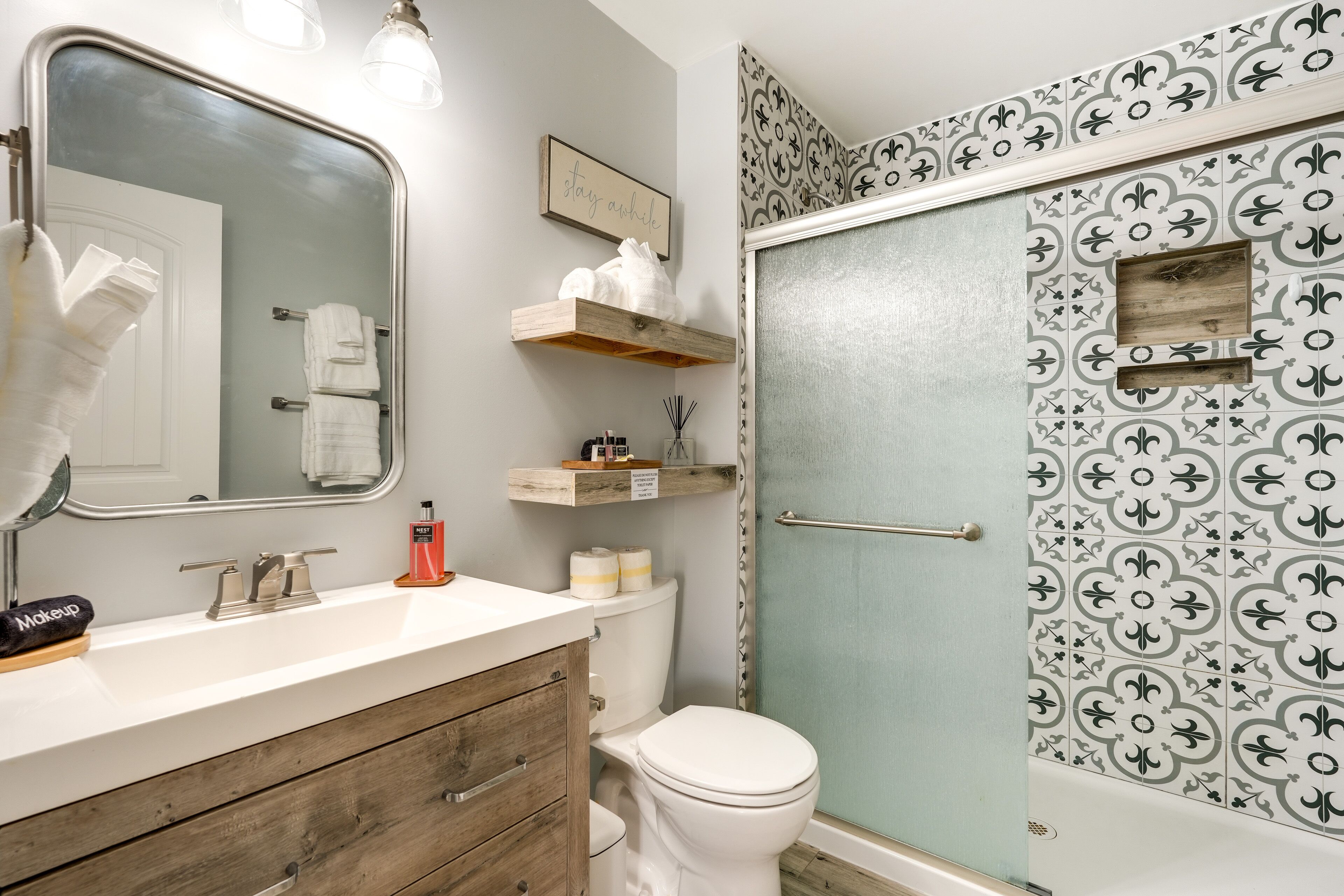A bathroom with a white sink, wooden vanity, a large mirror, a toilet, and a shower with patterned tiles.