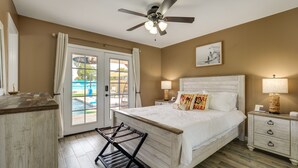 A bedroom with a bed, nightstands, a ceiling fan, a window with curtains, and a view of a pool. - Glendale Getaway: Swim, Putt, Grill, & Relax! (Glendale)