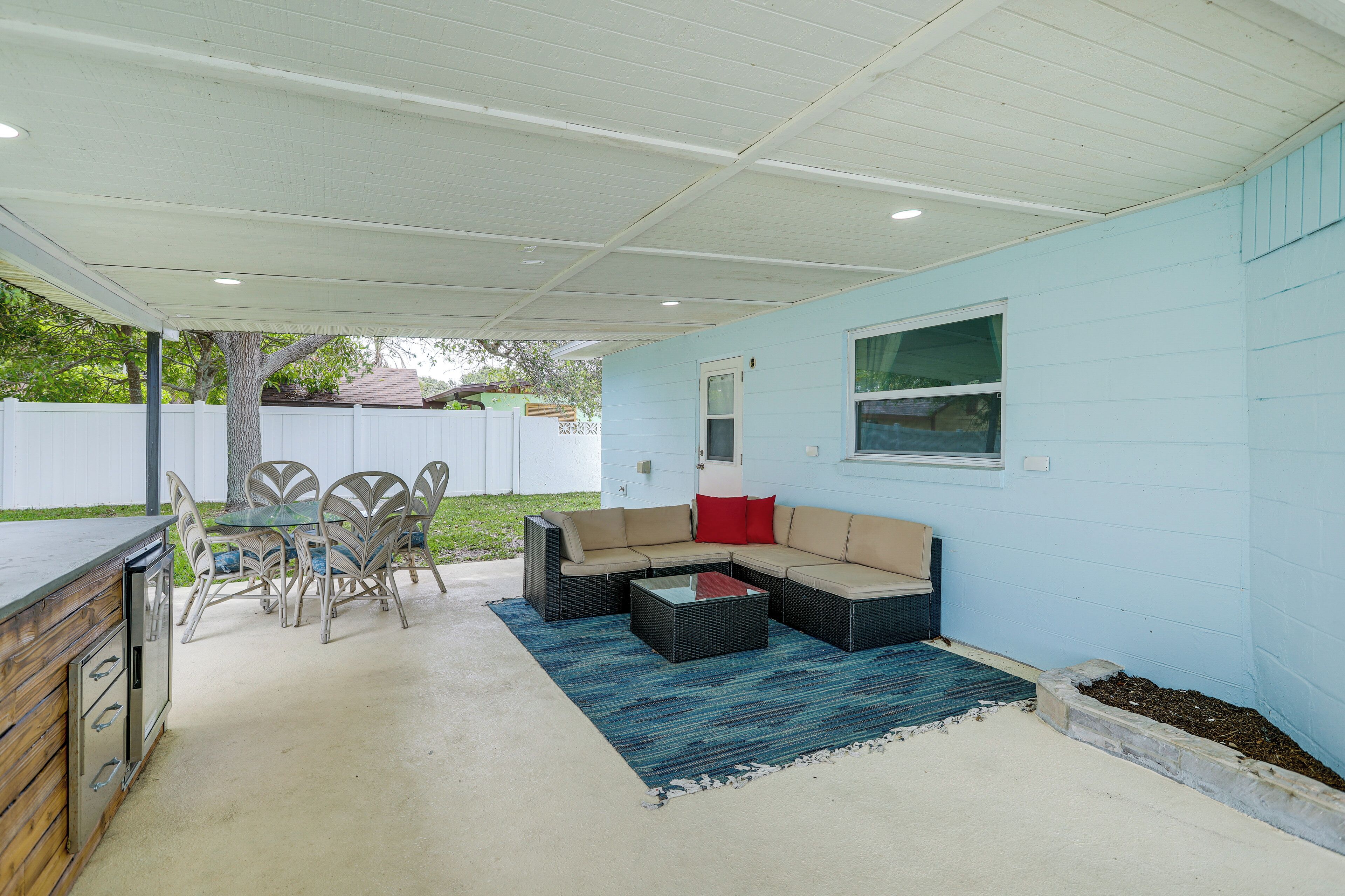 A covered patio with a dining area, a built-in grill, and a seating arrangement.