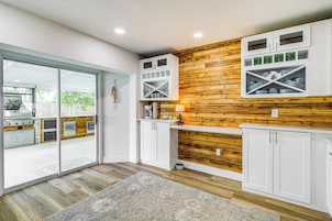 Una cocina moderna con armarios blancos, una pared de acento de madera y un portón corredizo de vidrio que da a un patio.