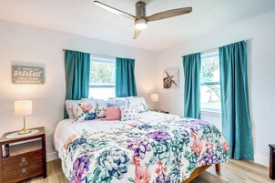 Un dormitorio con una cama, dos mesitas de noche, un ventilador de techo y cortinas color turquesa.