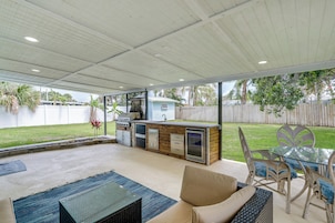 Un patio al aire libre con una mesa de vidrio, muebles de mimbre y una barbacoa integrada.