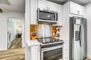 Una cocina moderna con armarios blancos, un microondas de acero inoxidable, un horno empotrado y un refrigerador.
