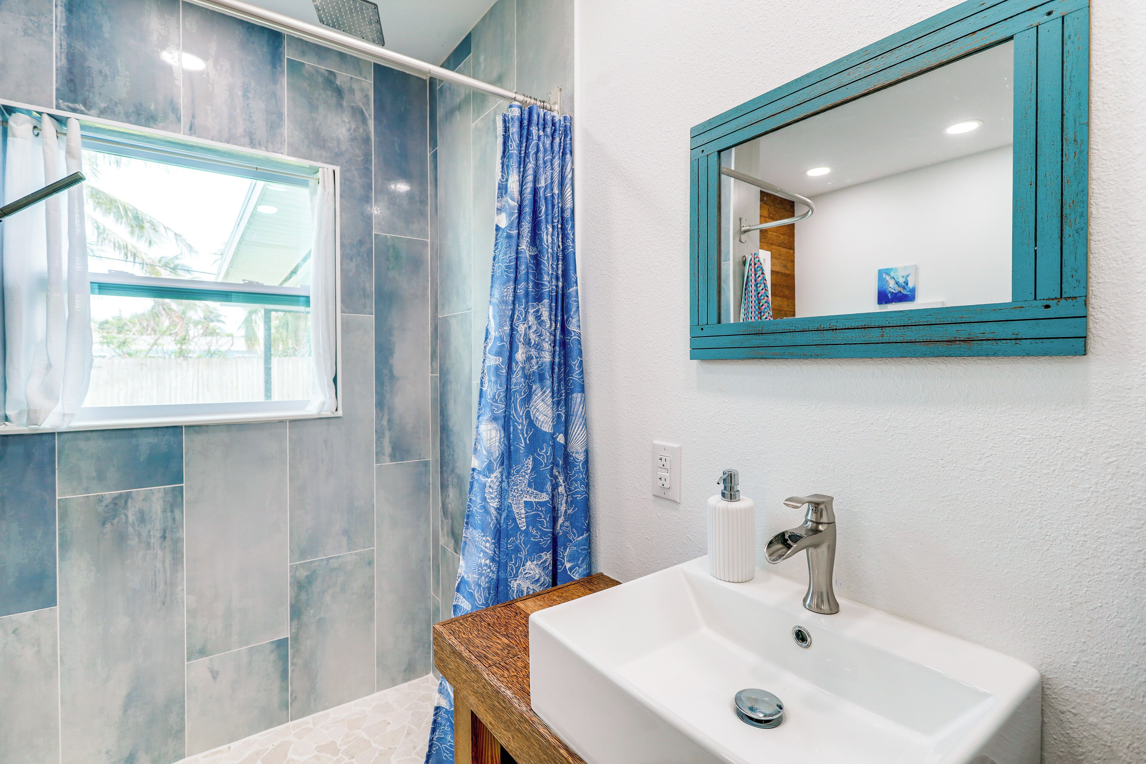 A bathroom with a shower, a window, a sink, and a mirror.