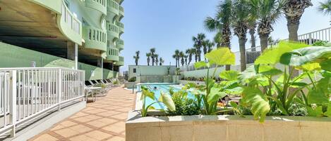 A pool area with a tiled floor, surrounded by palm trees and a building with balconies.