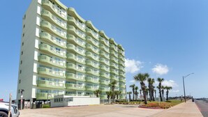 Un hotel de varios pisos con balcones, un estacionamiento y palmeras.