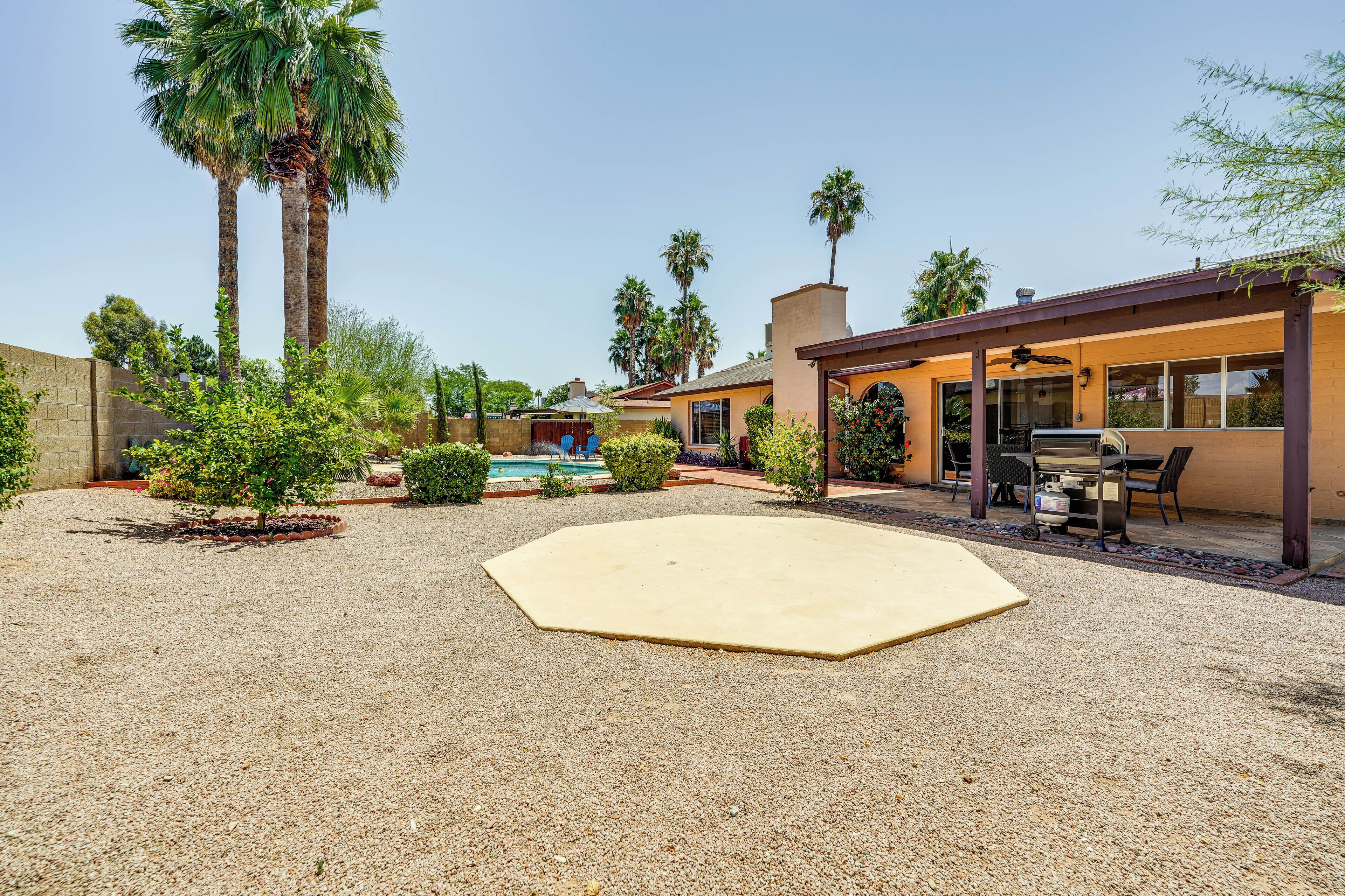 A backyard with a swimming pool, palm trees, and a barbecue area.