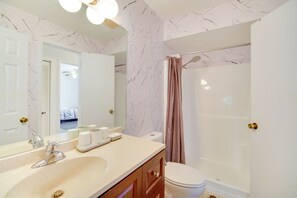 A bathroom with a marble-patterned wall, a sink with a mirror, a toilet, and a shower with a curtain. - Family-friendly Home on Lake Tulane: Great Views! (Avon Park)