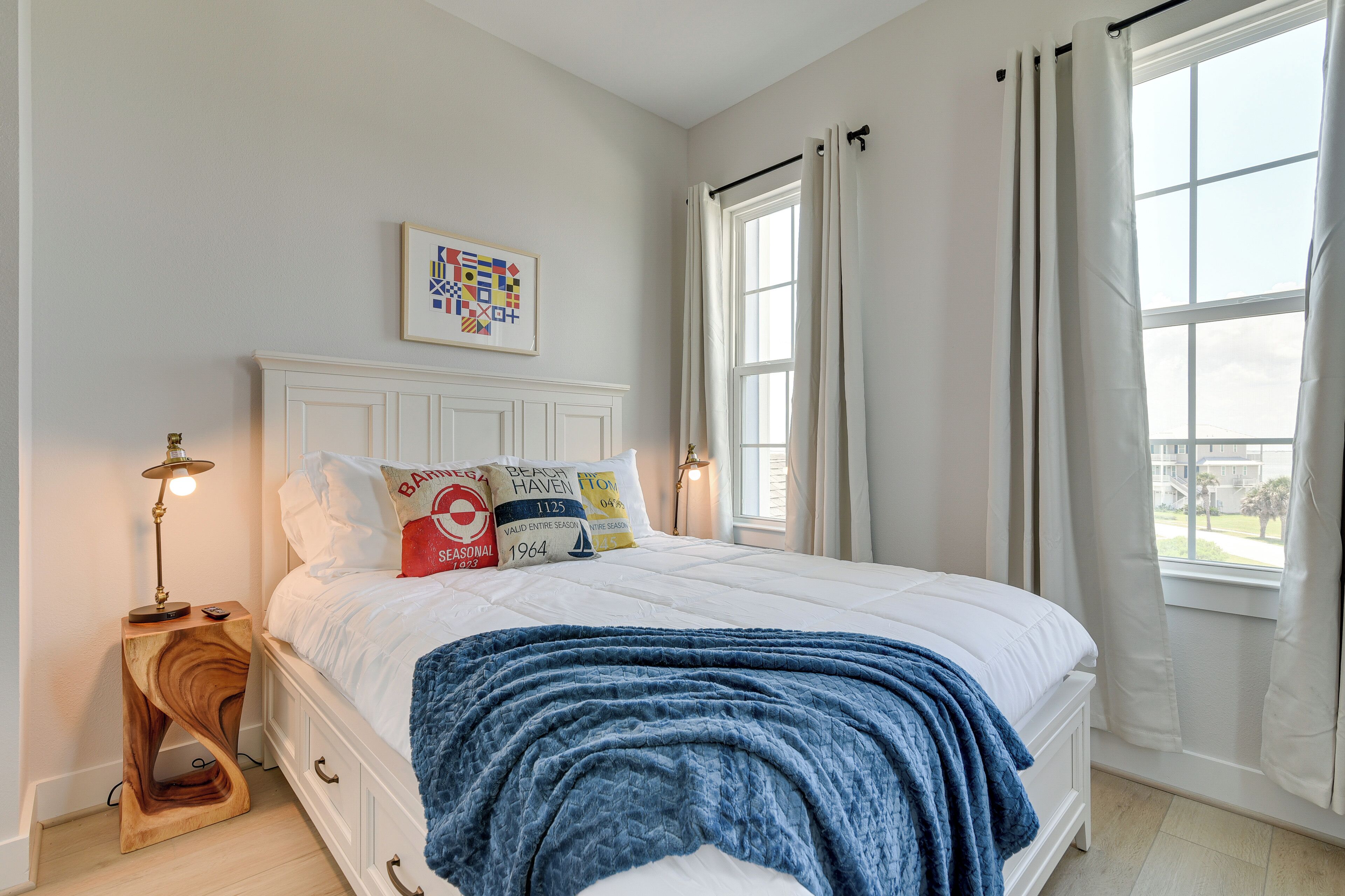 Una camera da letto con un letto bianco, un comodino in legno, una lampada e una finestra con tende.