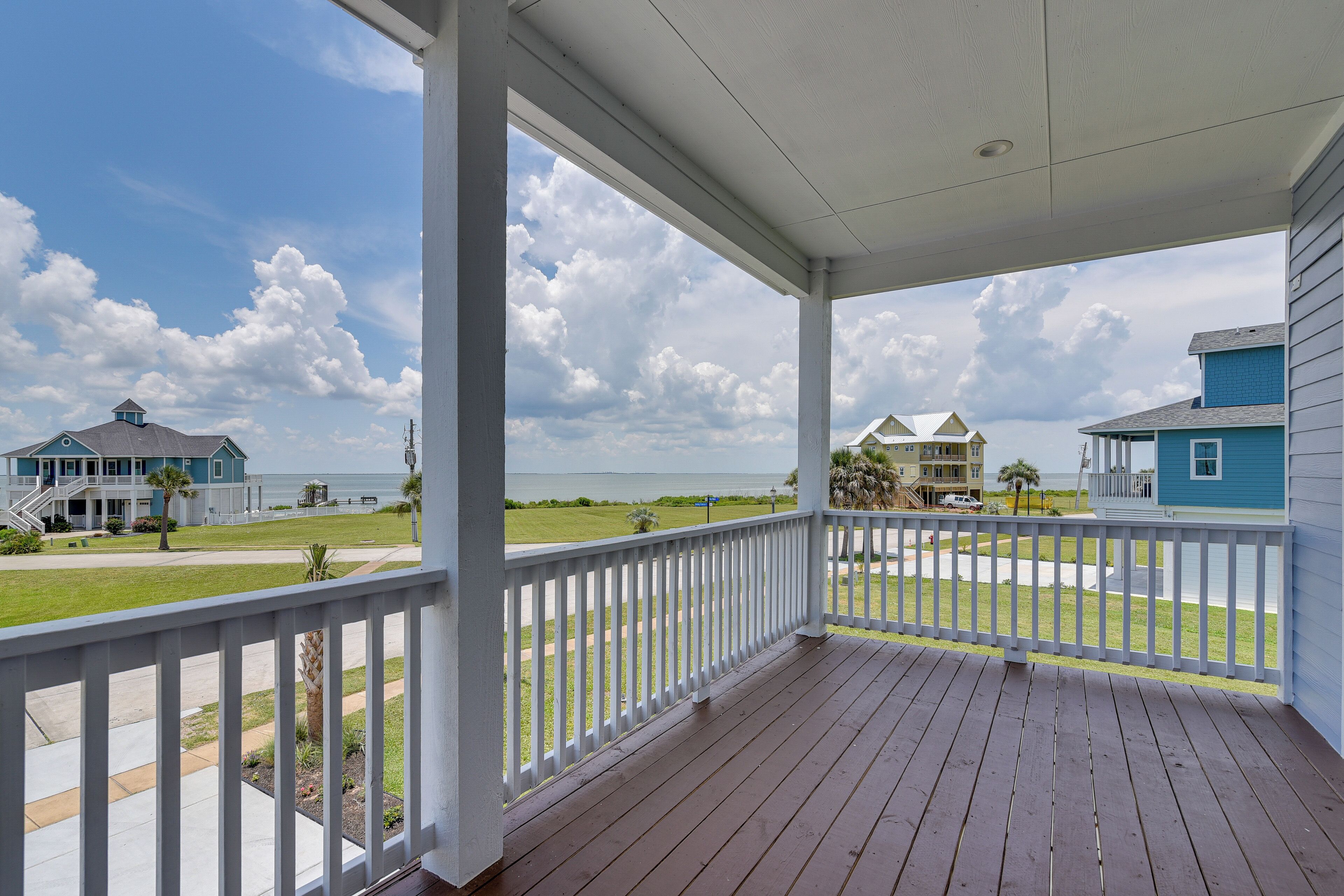 A covered porch with a view of a beach and houses.