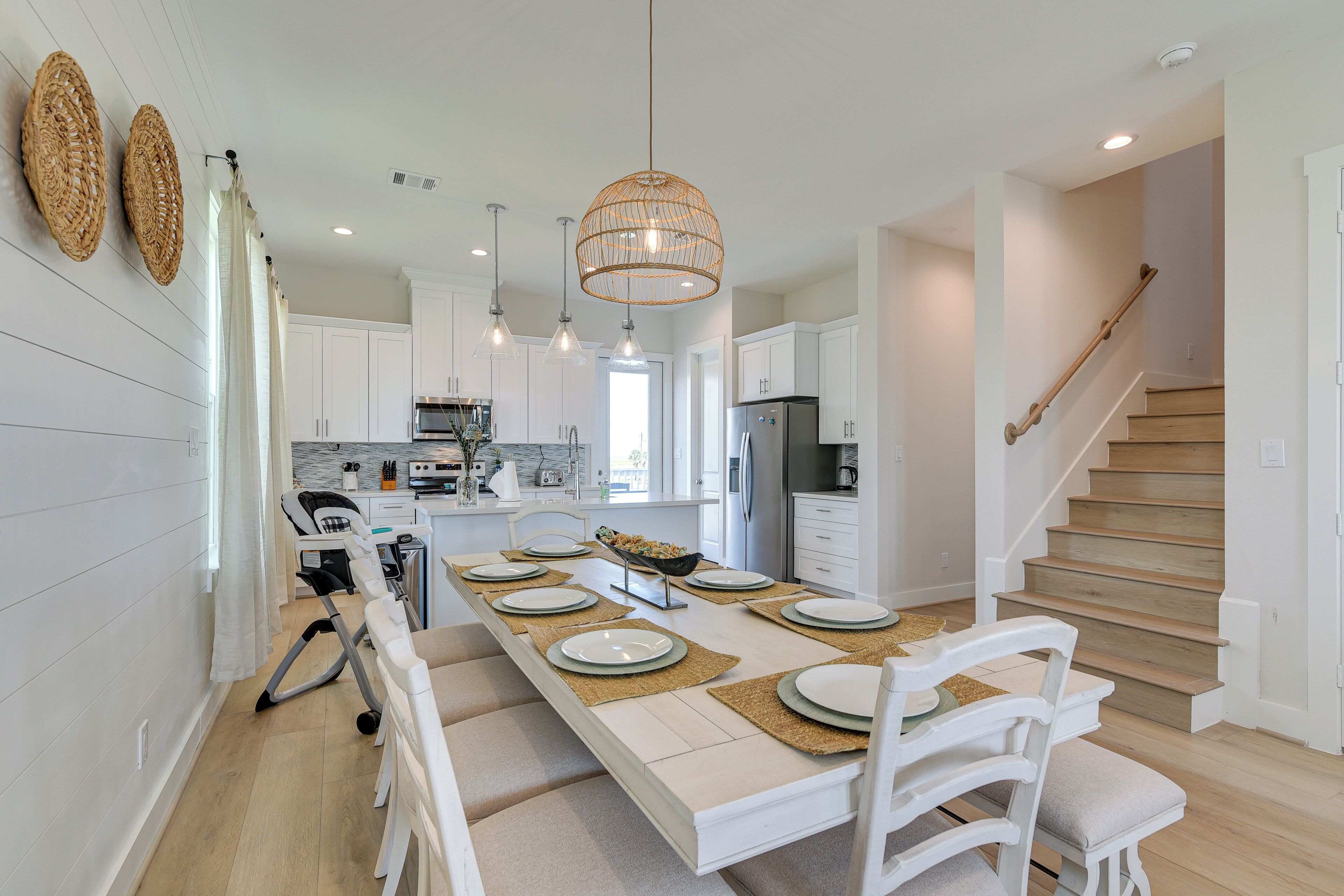 A modern kitchen with white cabinetry, a dining area set for six, and a wooden staircase.