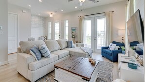 A spacious living room with a beige sectional sofa, a blue armchair, a wooden coffee table, and a ceiling fan. - 'seas The Day:' Home w/ Pool Access in Galveston (Galveston)