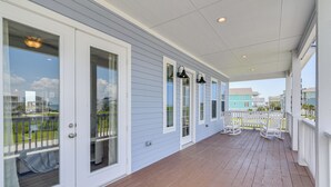 A covered porch with a wooden deck, white railings, and a view of neighboring buildings. - 'seas The Day:' Home w/ Pool Access in Galveston (Galveston)