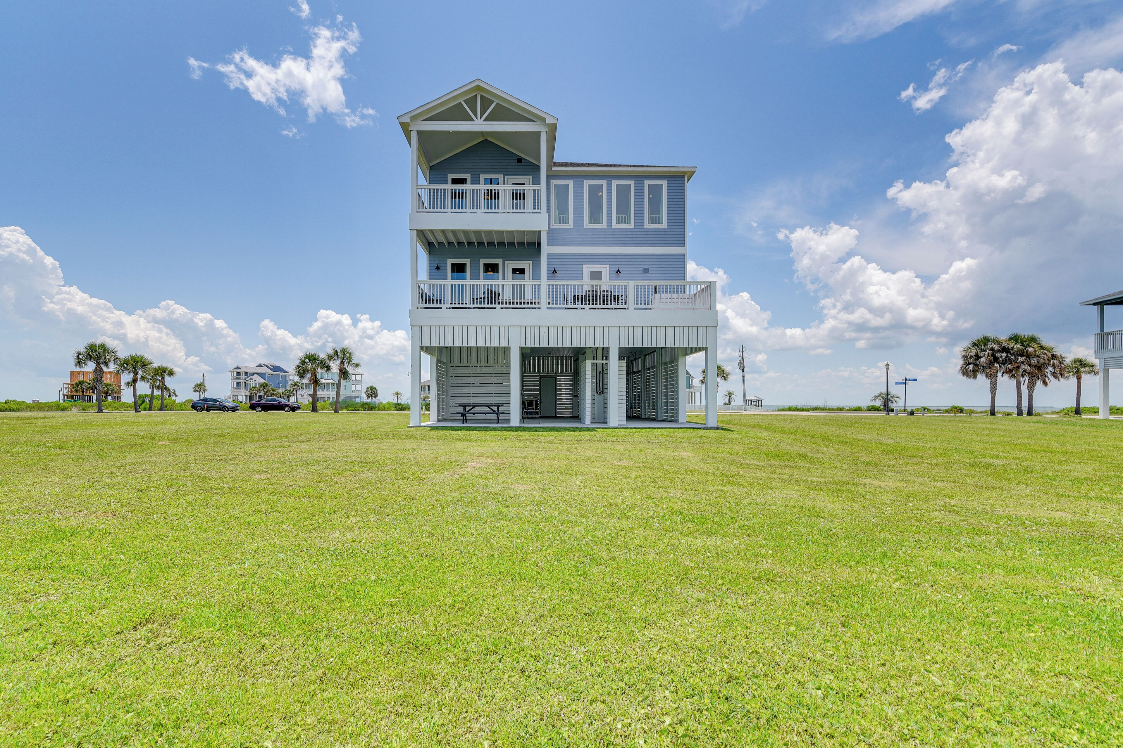 A two-story beachfront house with a balcony on the upper floor and a covered porch on the ground floor.