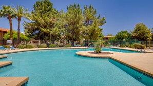 A swimming pool with clear blue water, surrounded by palm trees and a fenced area with lounge chairs. - Chandler Vacation Rental w/ Pool & Hot Tub Access (Chandler)