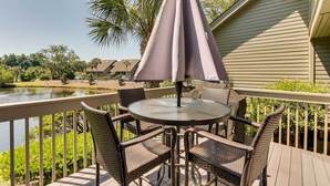 Une terrasse dotée d’une table ronde et de chaises en osier, offrant une vue sur une étendue d’eau et entourée de verdure.