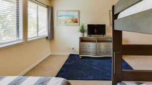 Une chambre avec un lit superposé, une télévision, une commode et un tableau représentant une scène de plage.