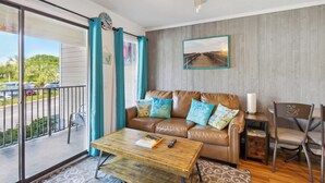 A living room with a leather sofa, teal cushions, a wooden coffee table, and a view of the street through a sliding glass door.