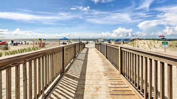 A wooden boardwalk leading to a beach with umbrellas and a sign indicating dune rebuilding.