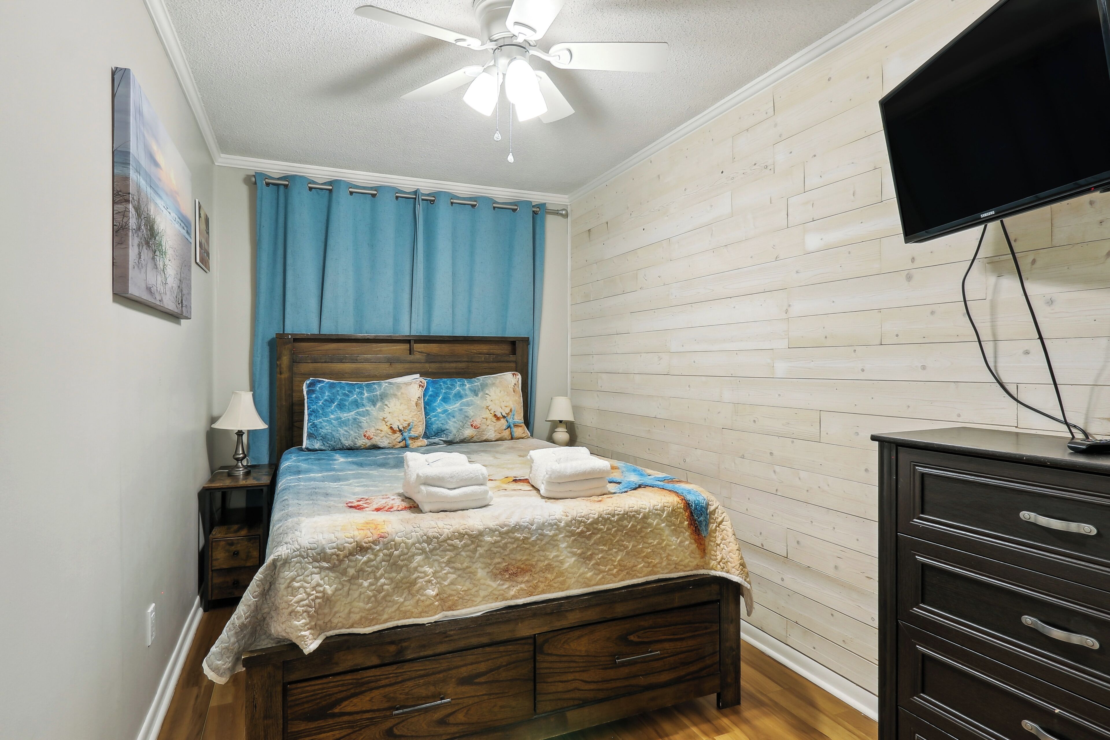 Een slaapkamer met een houten bed, een plafondventilator, een aan de muur bevestigde televisie en een houten dressoir.