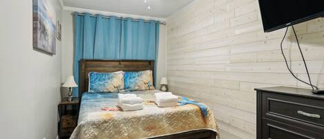 Een slaapkamer met een houten bed, een plafondventilator, een aan de muur bevestigde televisie en een houten dressoir.
