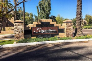 A sign for Signature Condominium Homes with a stone and brick entrance, surrounded by palm trees and a clear blue sky. - Near Westworld & TPC Golf: Scottsdale Gem w/ Pool (Scottsdale)
