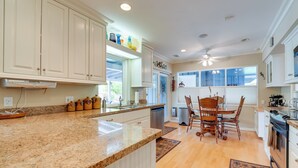 A kitchen with granite countertops, white cabinetry, a dining area with wooden chairs, and a ceiling fan.
