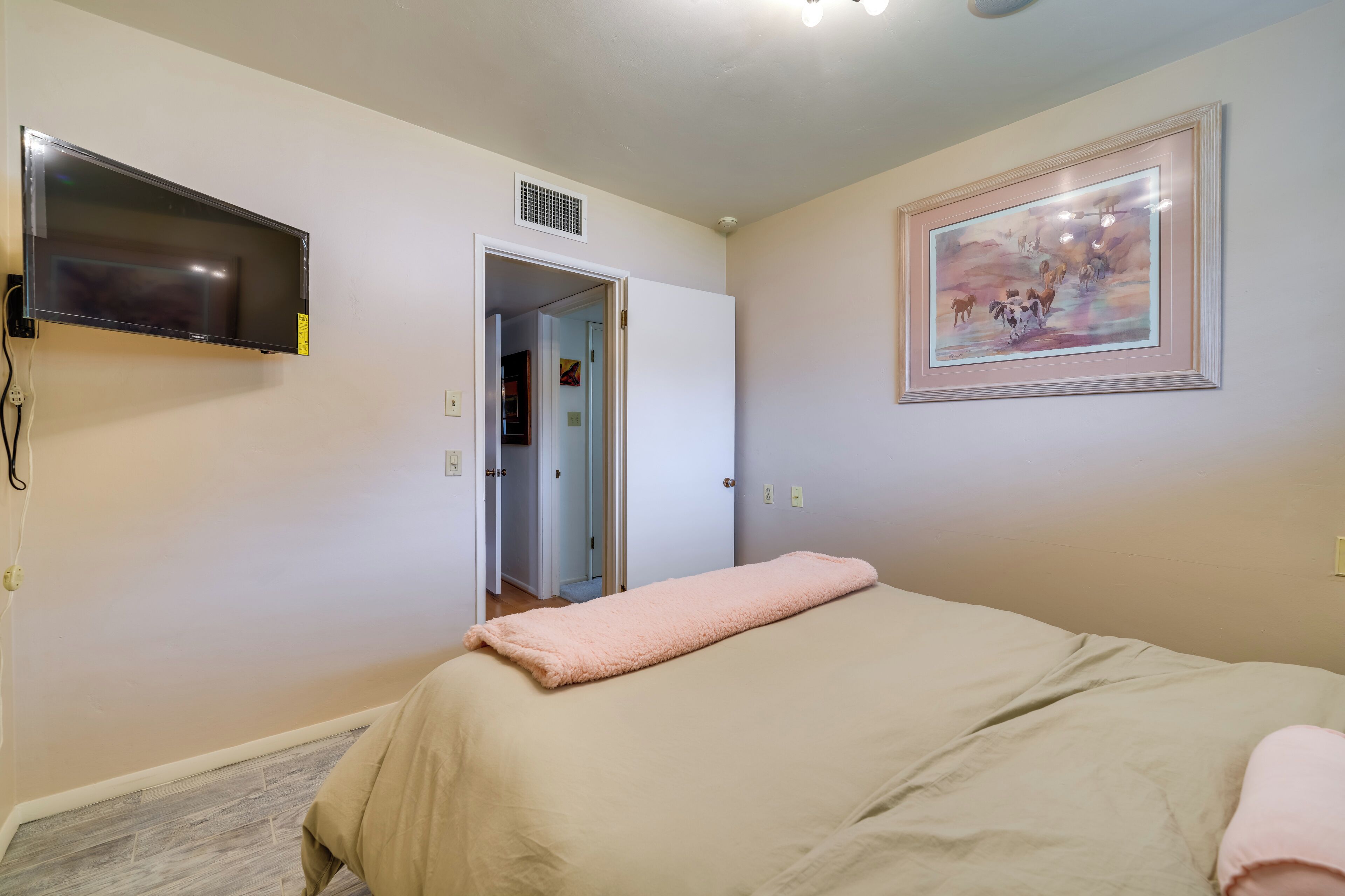 A bedroom with a bed, a TV mounted on the wall, and a door leading to another room.