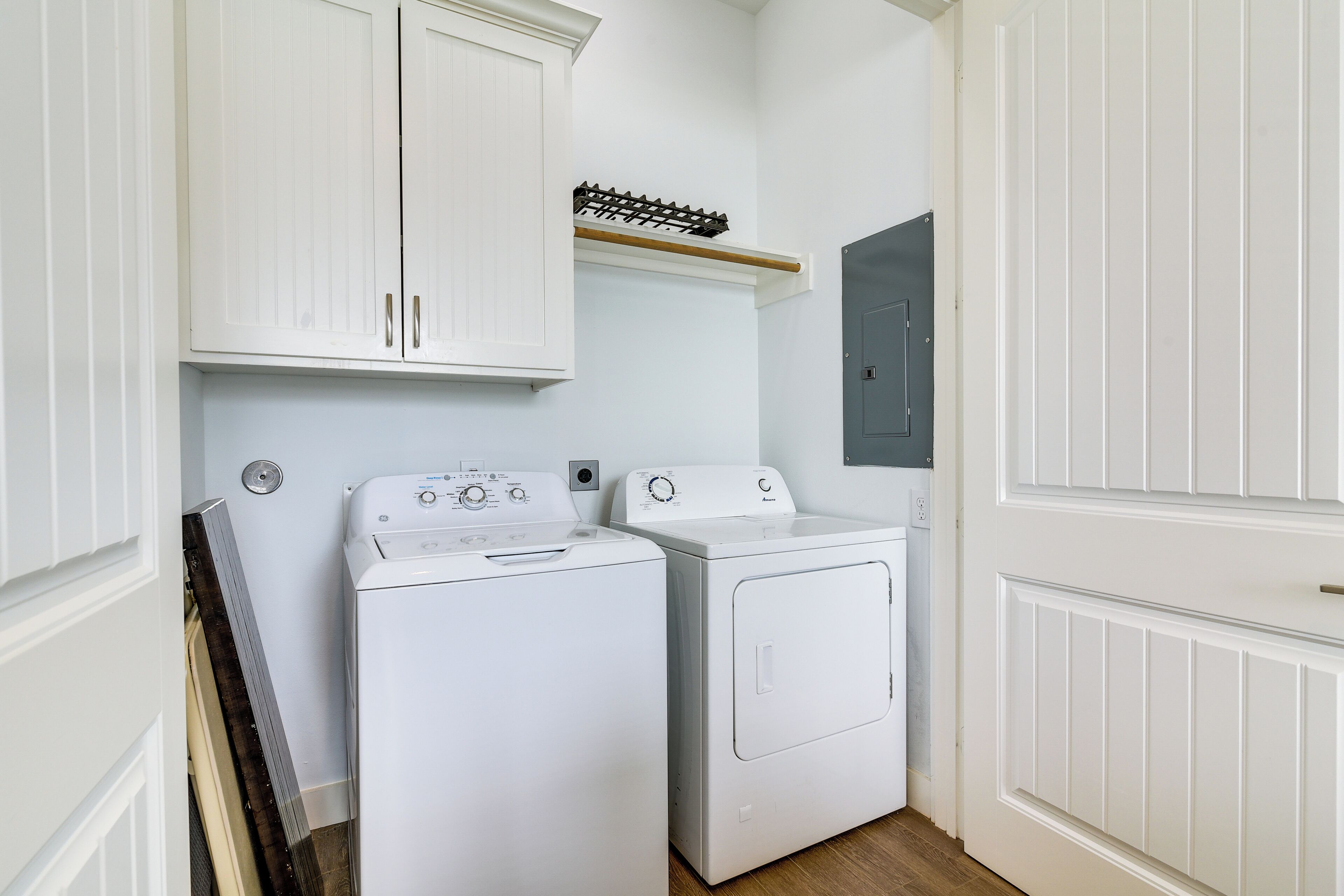 A laundry room with two white washing machines, a drying rack, and a grey door.