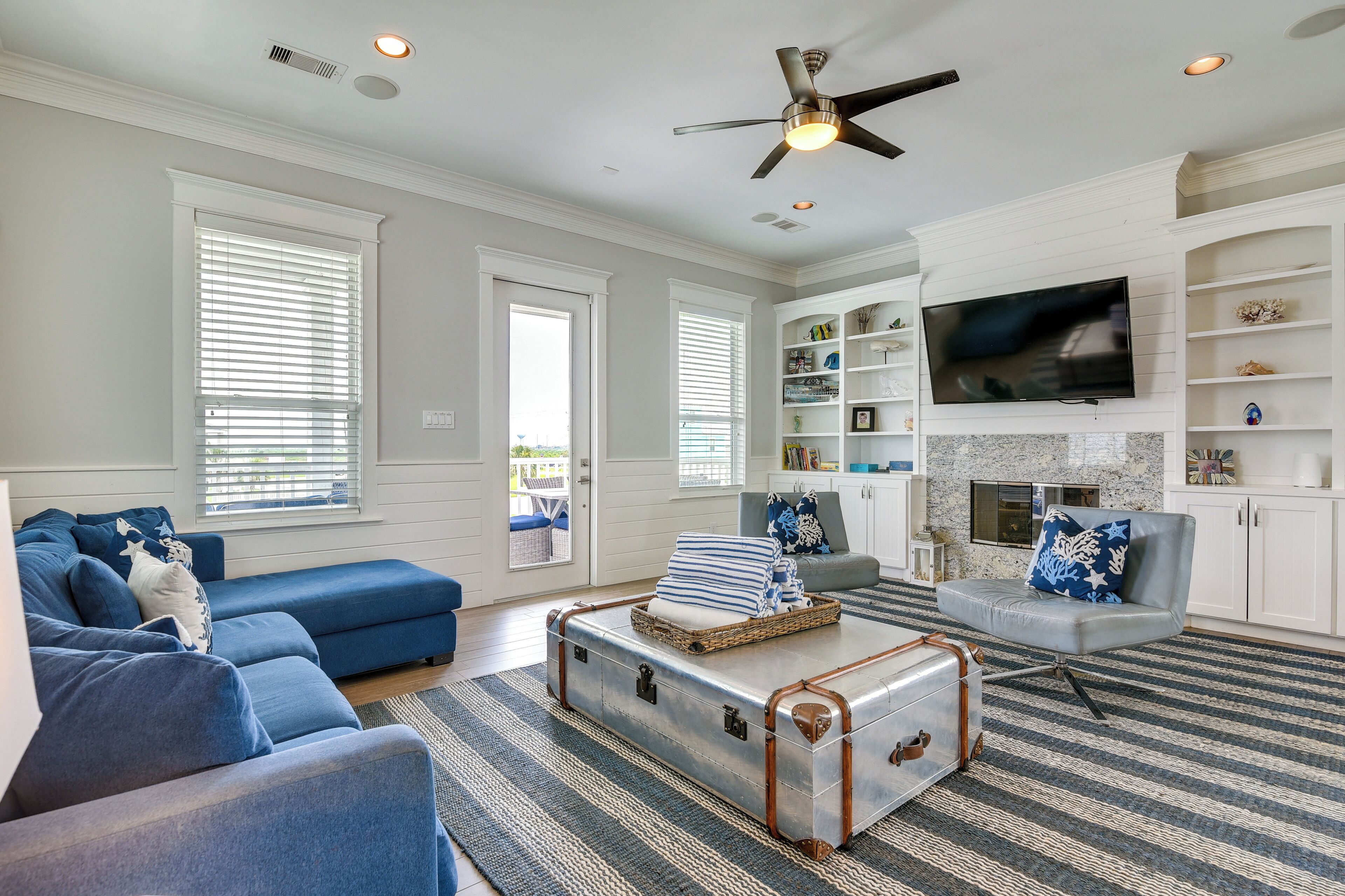 A living room with a blue sofa, a grey armchair, a white fireplace, and a television mounted on a white cabinet.