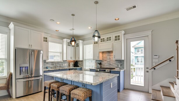 A modern kitchen with a central island, stainless steel appliances, and a staircase leading to a balcony. - Walk to Ocean! Group Beach House in Galveston (Galveston)