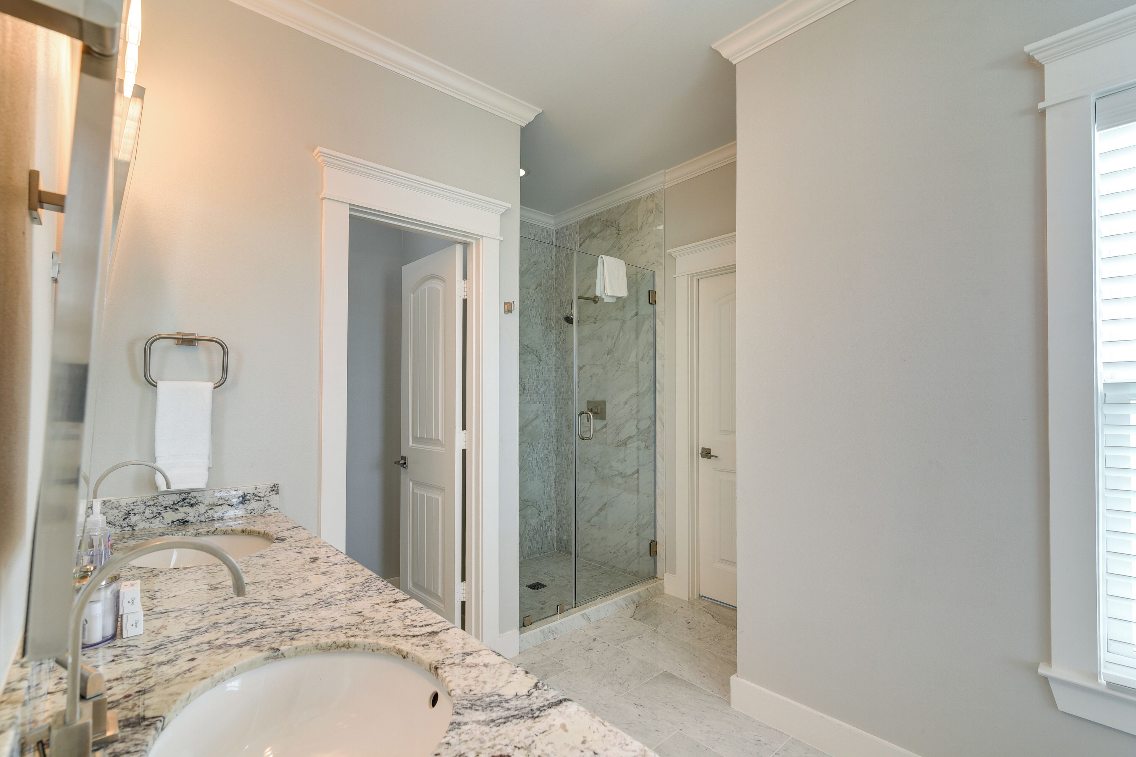A bathroom with a marble vanity, a glass shower enclosure, and a white door.