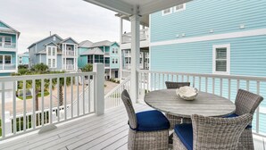 A covered outdoor area with wicker furniture and a round table, overlooking a row of blue buildings. - Walk to Ocean! Group Beach House in Galveston (Galveston)
