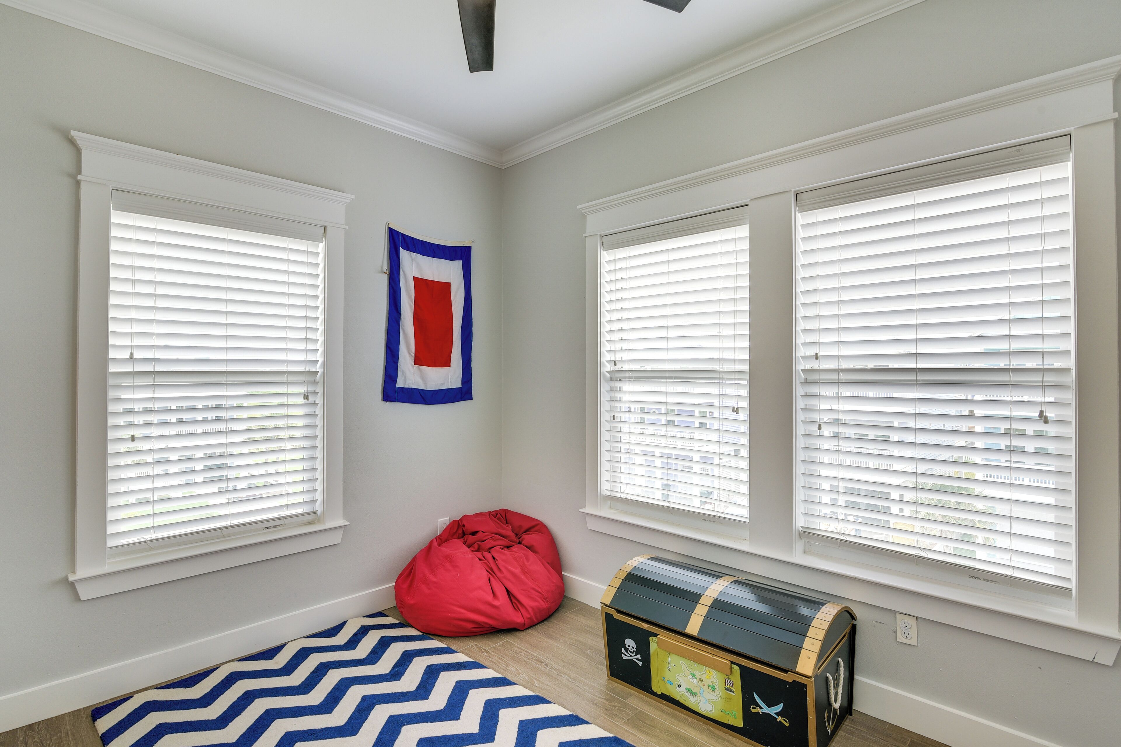A room with two large windows, a red bean bag, and a treasure chest.