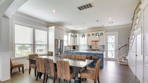 A spacious kitchen with a central island, white cabinetry, and a dining area with wicker chairs. - Walk to Ocean! Group Beach House in Galveston (Galveston)