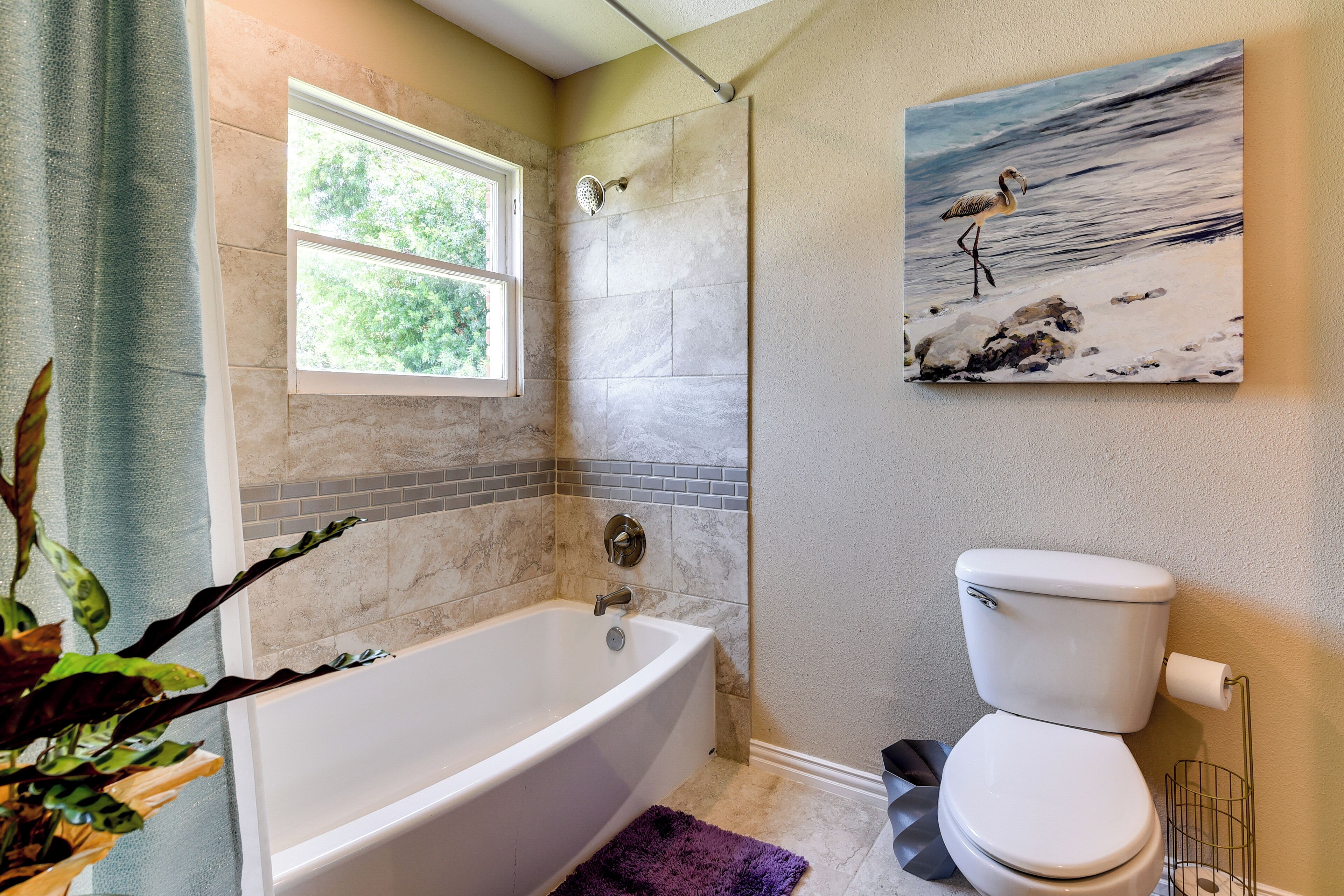 A bathroom with a bathtub, toilet, and a window.