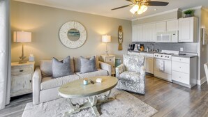 A modern living room with a sofa, armchair, and coffee table. A kitchen with white cabinets and appliances is visible in the background. - Top-floor Condo w/ Ocean Views in Hilton Head! (Hilton Head Island)
