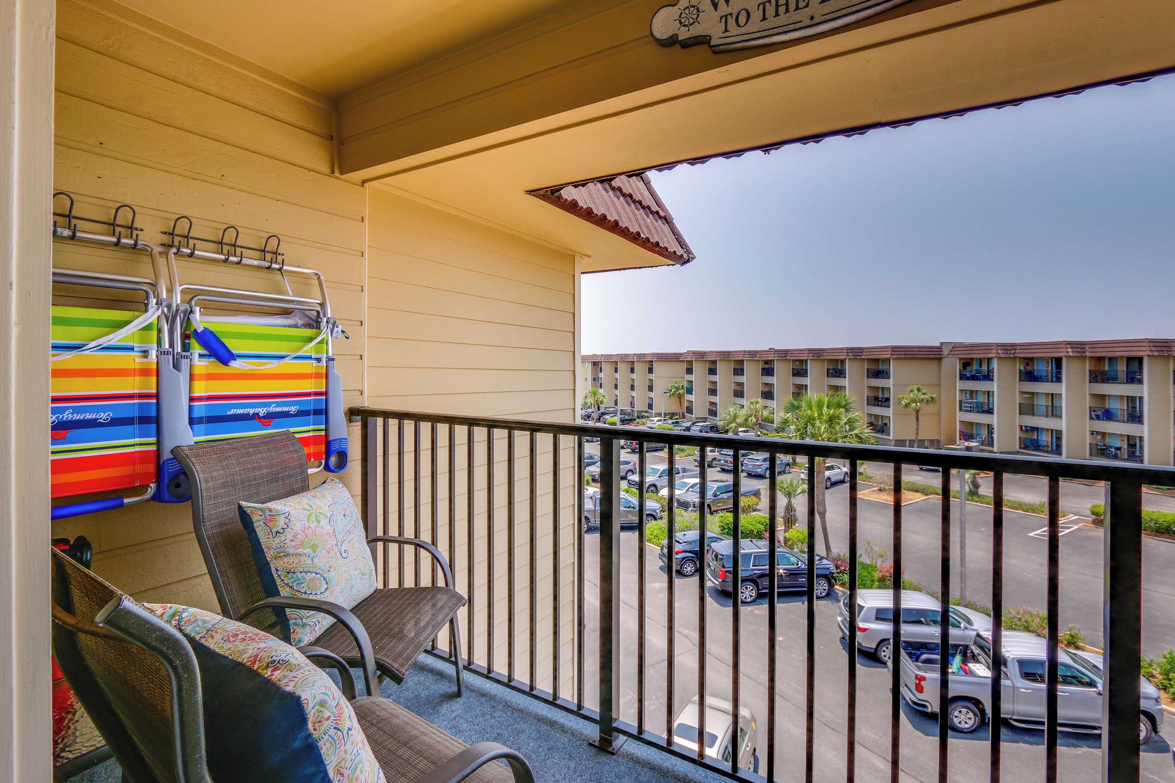 A balcony with chairs and a view of a parking lot and buildings.
