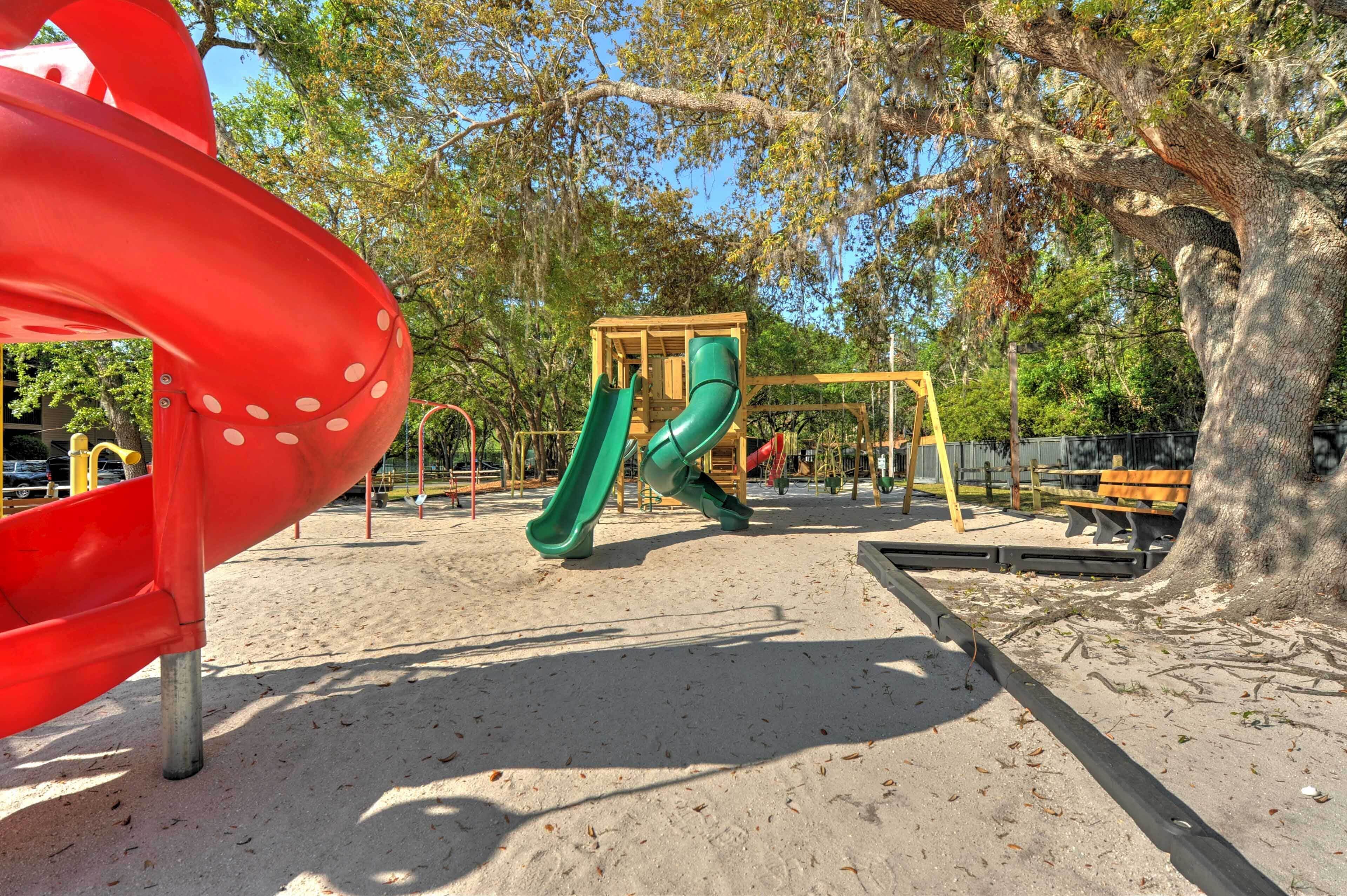 Un parque infantil con un tobogán rojo, toboganes verdes y una estructura de madera para escalar.