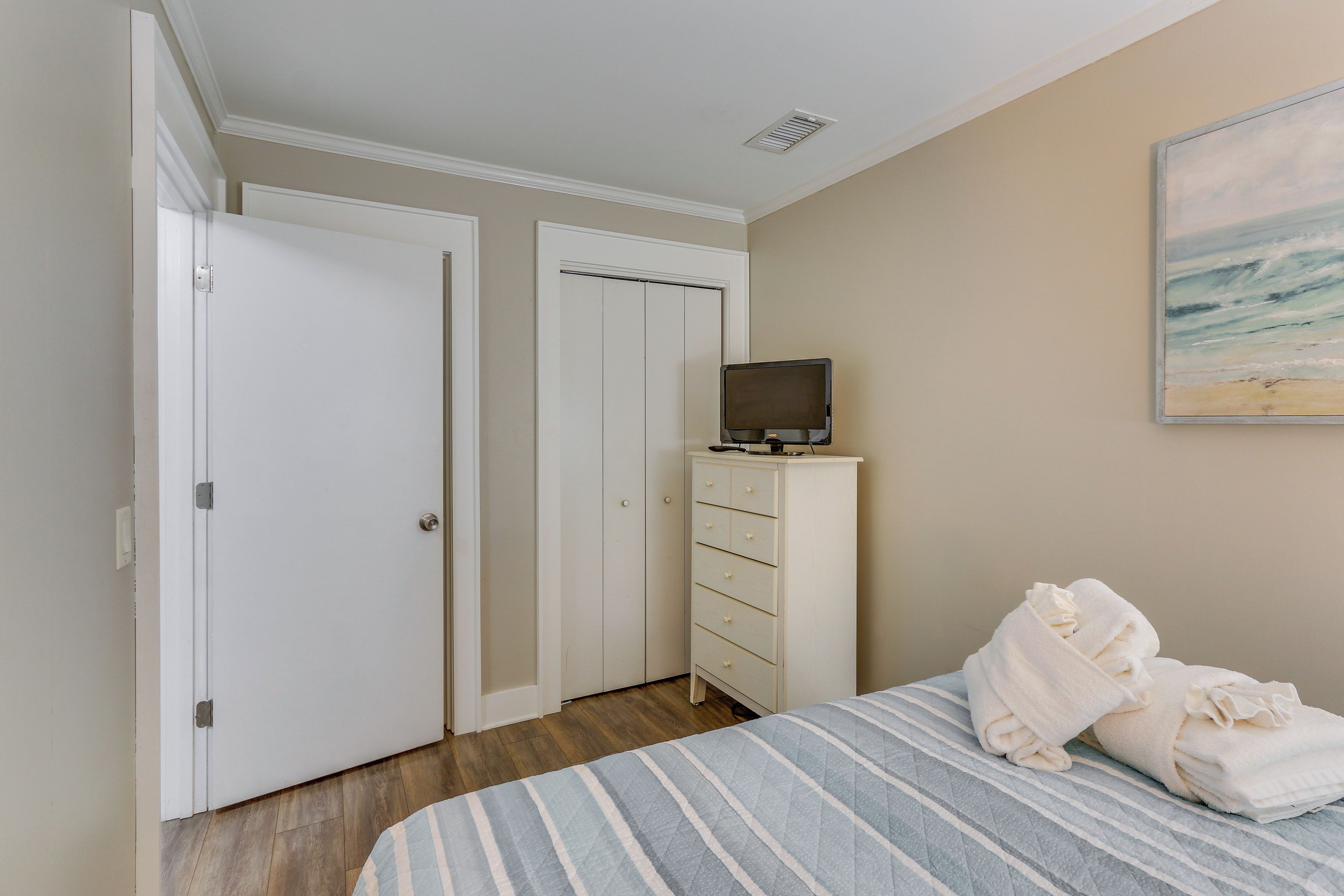 Une chambre à coucher avec un lit, un téléviseur posé sur une commode et un tableau accroché au mur.