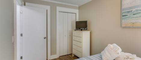 Une chambre à coucher avec un lit, un téléviseur posé sur une commode et un tableau accroché au mur.