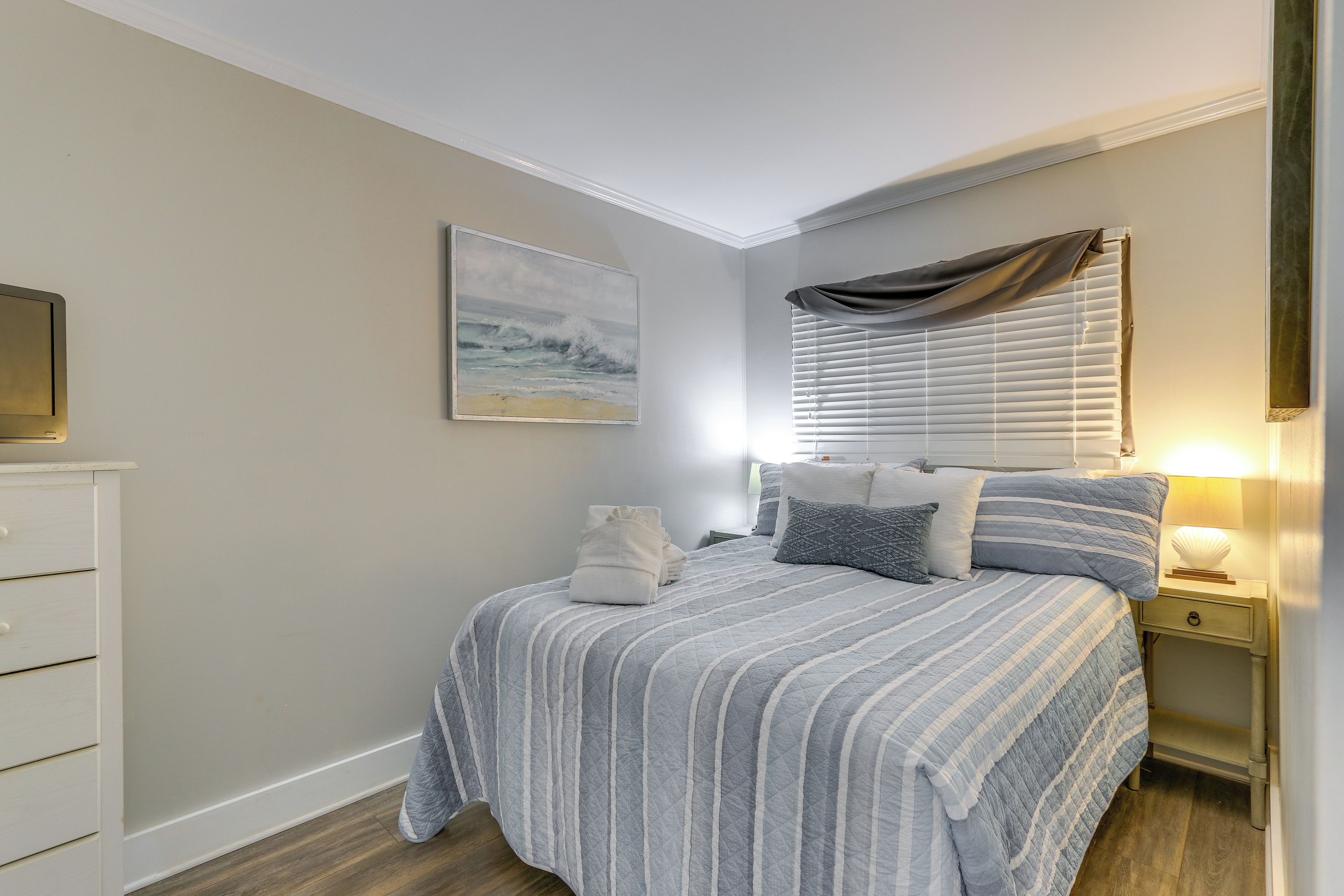 A neatly arranged bedroom with a bed, bedside tables, and a painting on the wall.