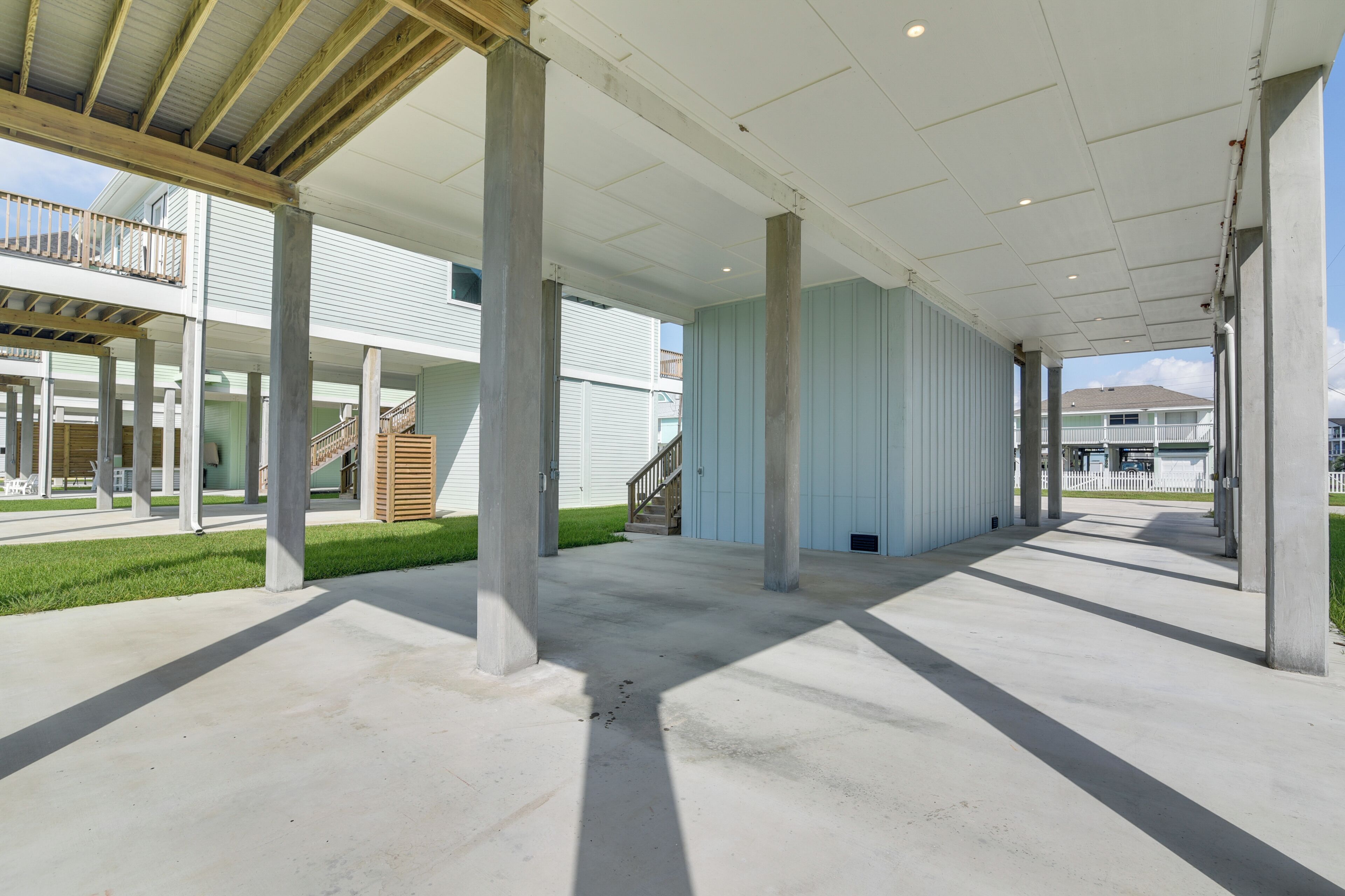 Un'area patio coperta e aperta, con pavimento in cemento, sostenuta da pilastri in cemento e vista su un edificio residenziale sullo sfondo.