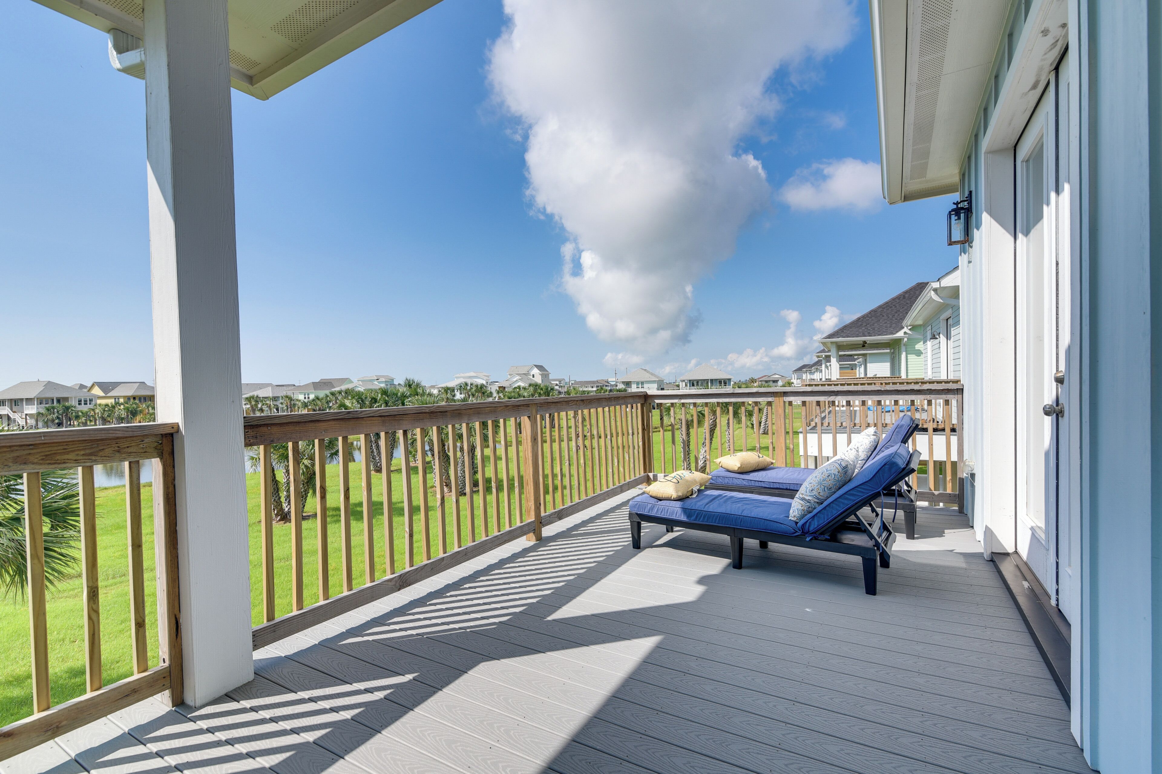 A covered outdoor deck with two lounge chairs and a wooden railing.