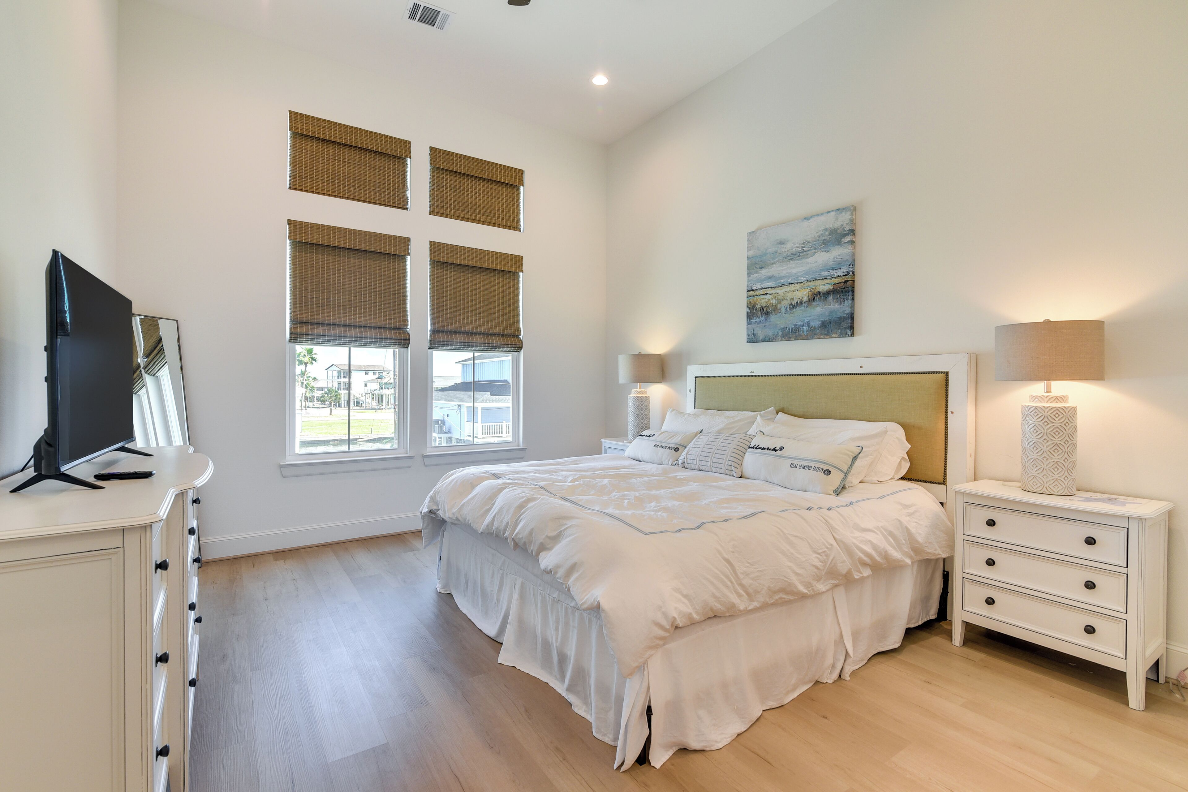 A bedroom with a large bed, bedside lamps, a nightstand, and a TV on a dresser.