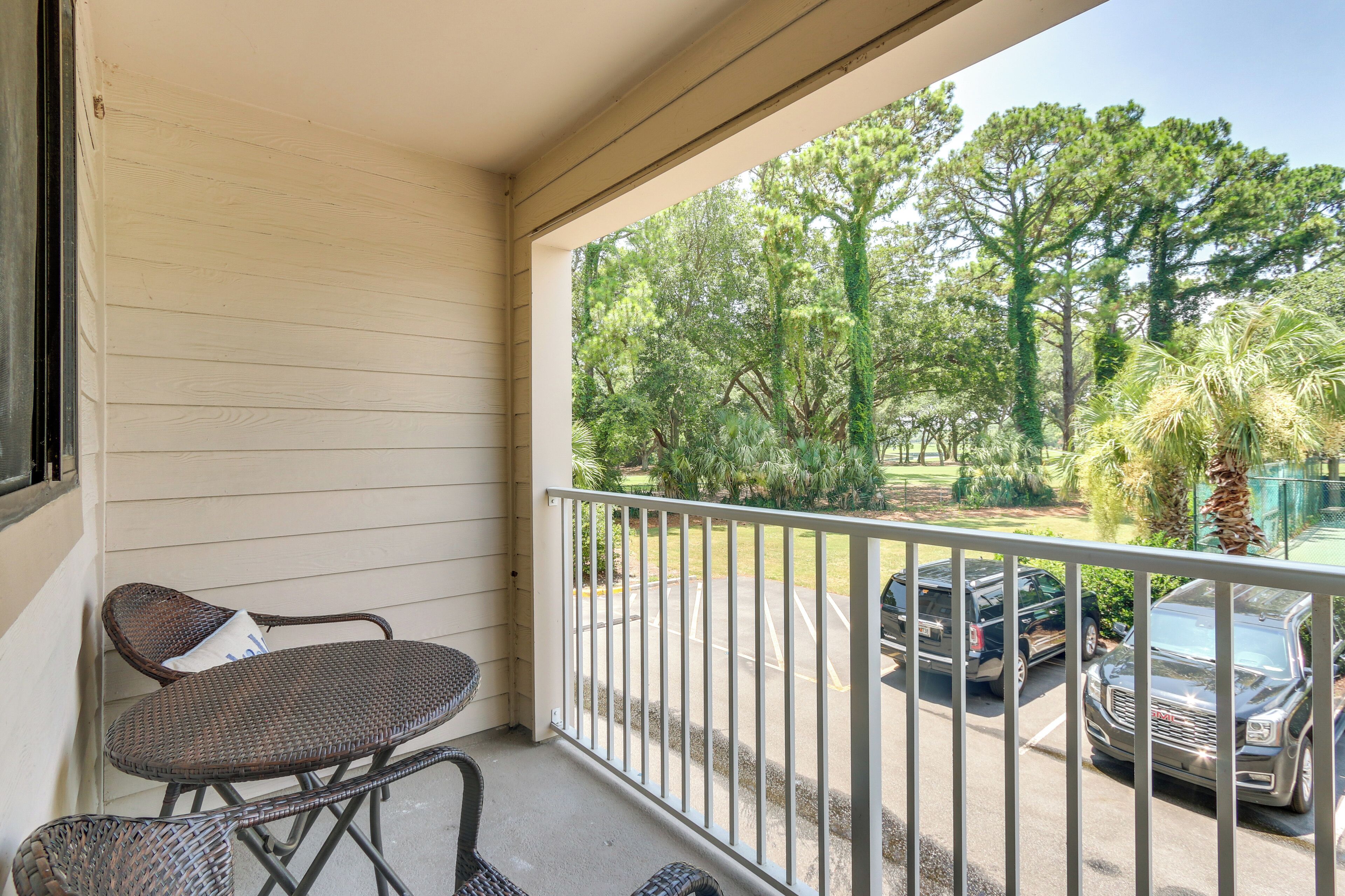 A balcony with wicker furniture and a view of parked cars and trees.