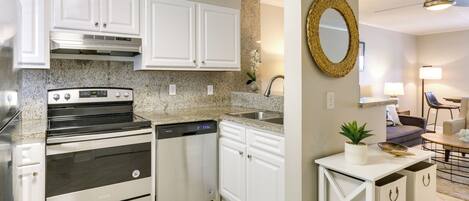 A modern kitchen with white cabinets, a granite countertop, stainless steel appliances, and a dining area with a table and chairs.