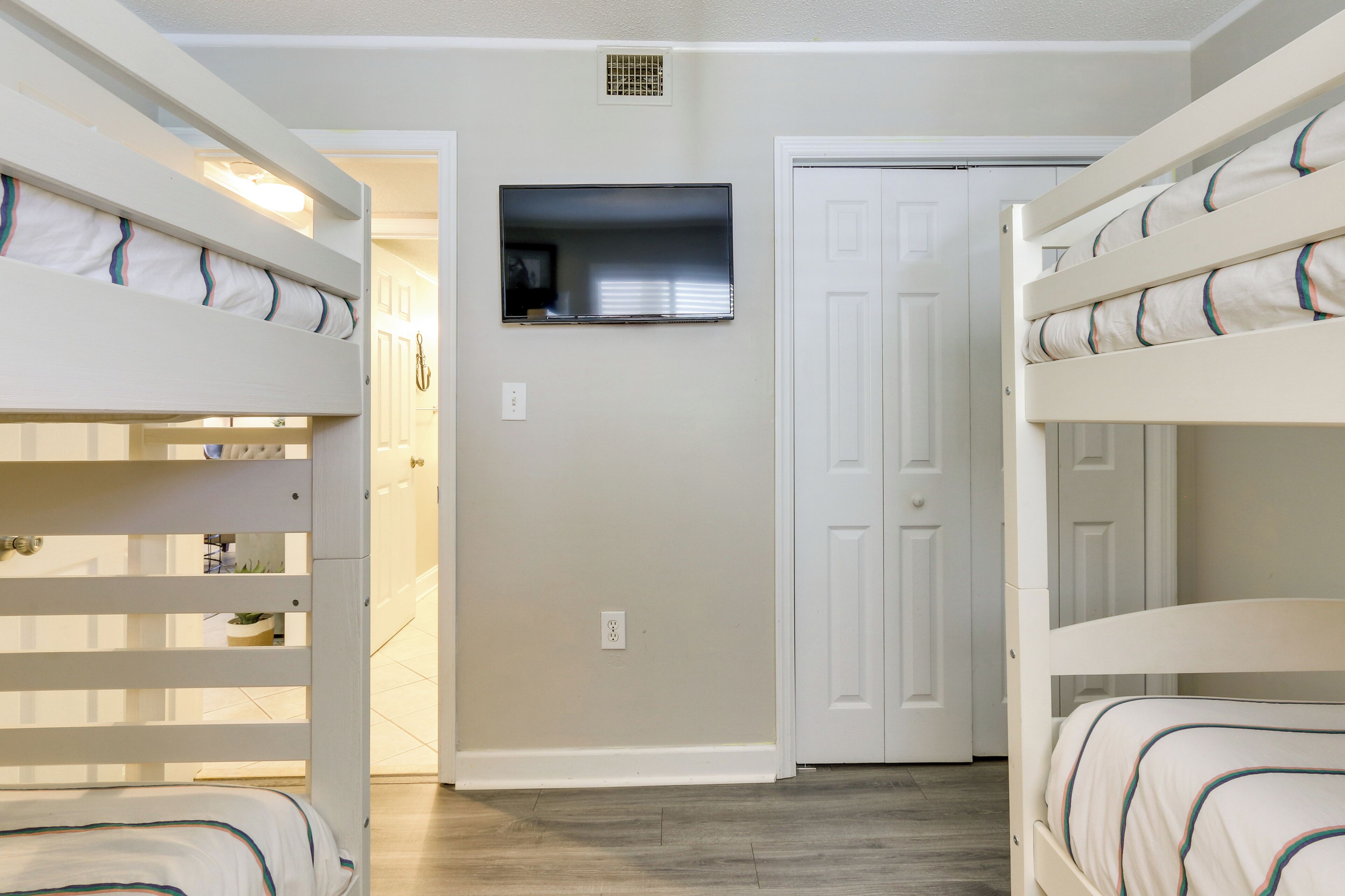 A room with bunk beds, a television mounted on the wall, and a door leading to another room.